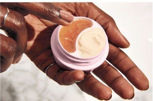 A person holding a jar of cream on their hand.